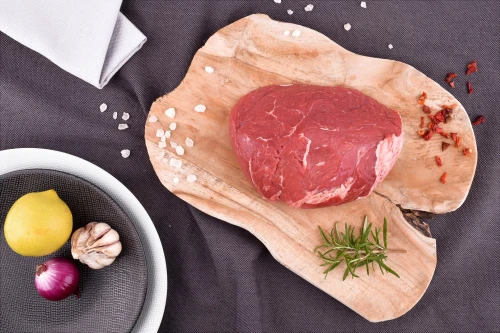Surowy udziec wołowy EKO 500g na drewnianej desce z solą, chili, cytryną, rozmarynem, czosnkiem i cebulą