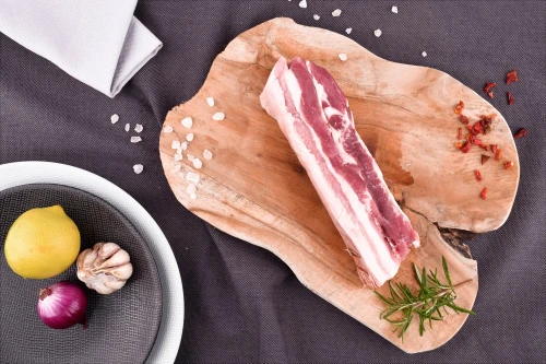 Surowy boczek EKO 500g na drewnianej desce z przyprawami i rozmarynem