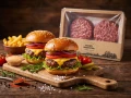 Burger wołowy BIO Farmy Roztocza — dwa gotowe cheeseburgery na drewnianej desce z frytkami i przyprawami, opakowanie w tle, aranżacja w stylu amerykańskim